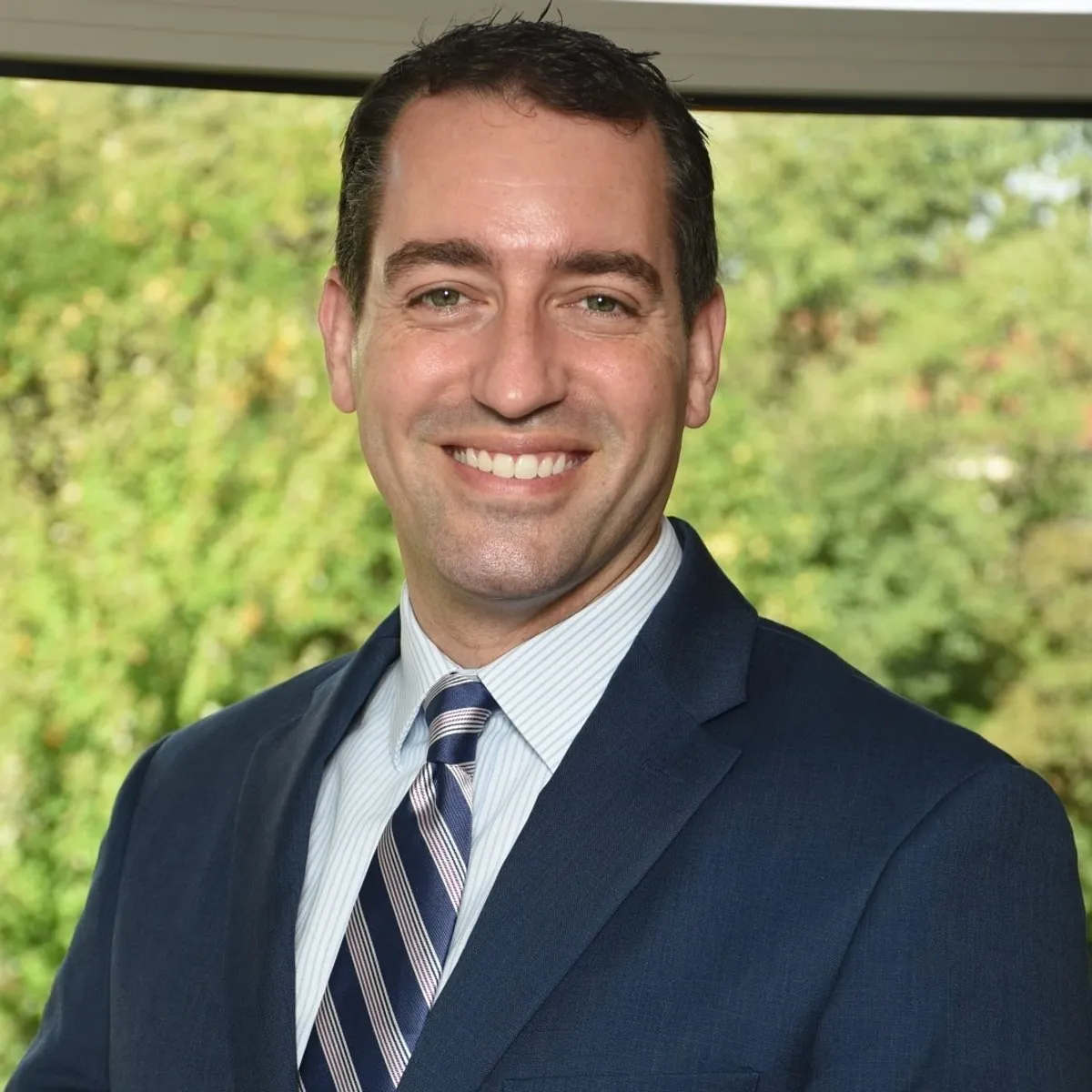 A man in a blue suit smiling outdoors.